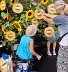 Ein Kind mit einem Rollator und eine Lehrerin schauen sich die Namen der neuen Schülerinnen und Schüler im Sonnenblumenkranz an.