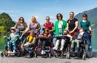Auf dem Bild sind fünf Schülerinnen, alle im Rollstuhl zu sehen. Sie posieren gemeinsam mit ihren sechs Lehr- und Betreuungspersonen vor der Bergkulisse in Iseltwald. Im Hintergrund ist der Brienzersee zu sehen.